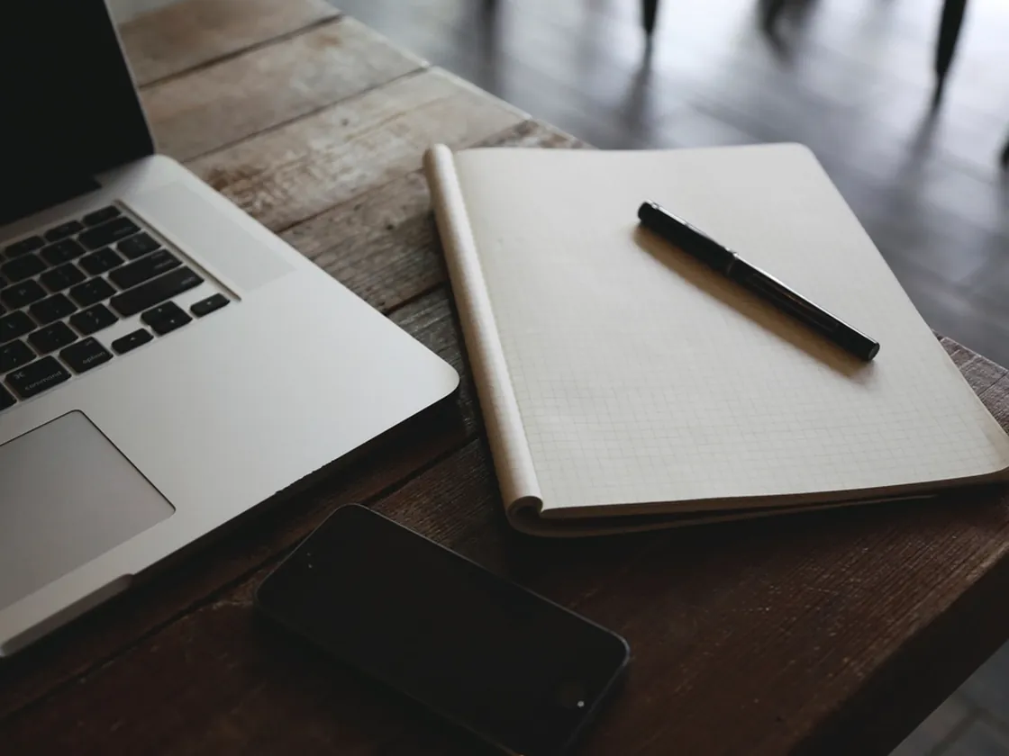 A notebook, pen and laptop on a wooden desk
