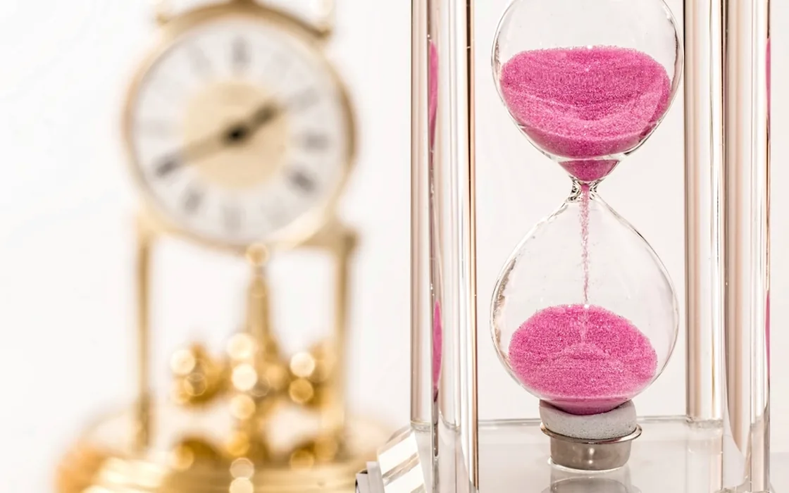 An hourglass with pink sand beside a small gold clock