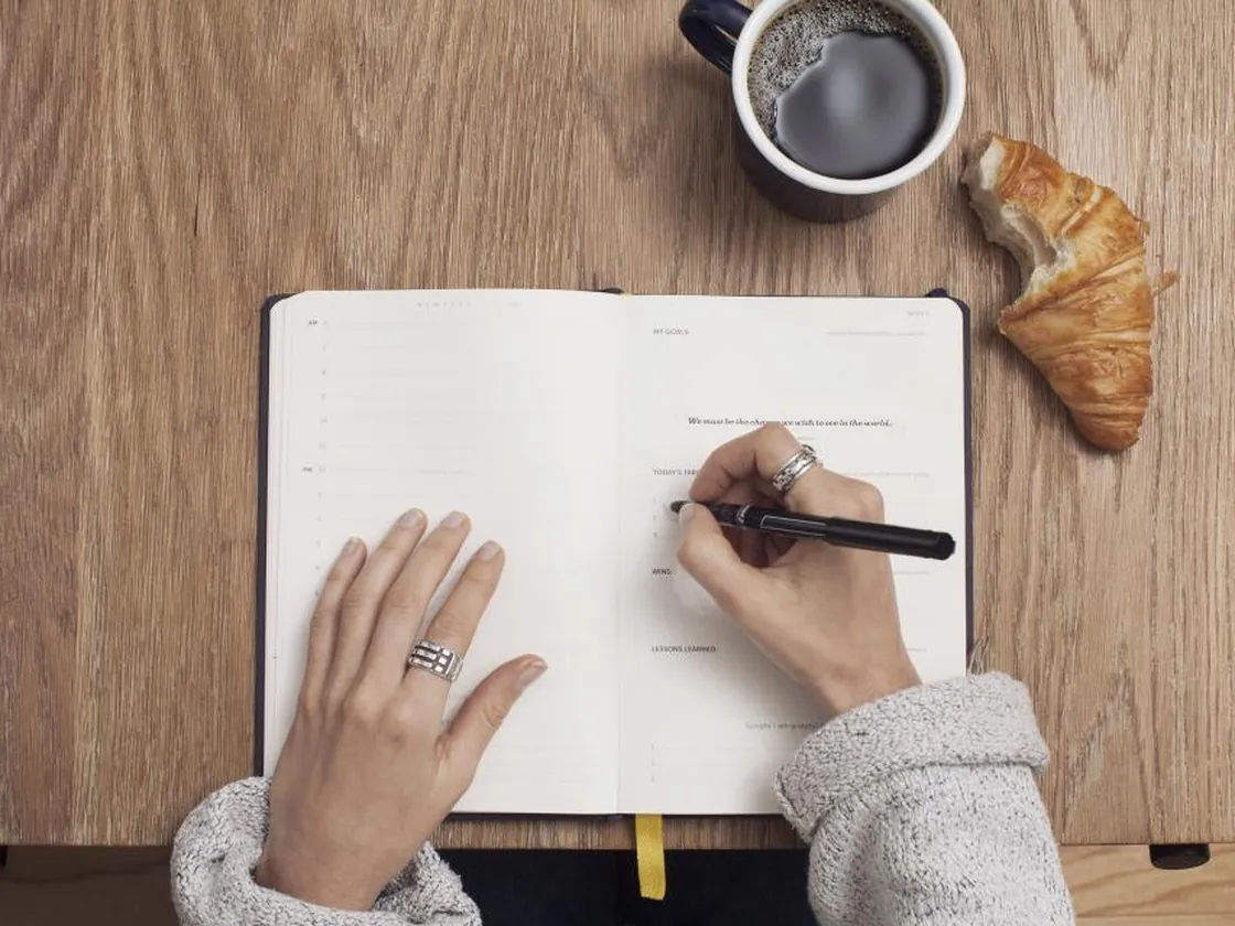 A hand writing in a notebook on a wooden desk
